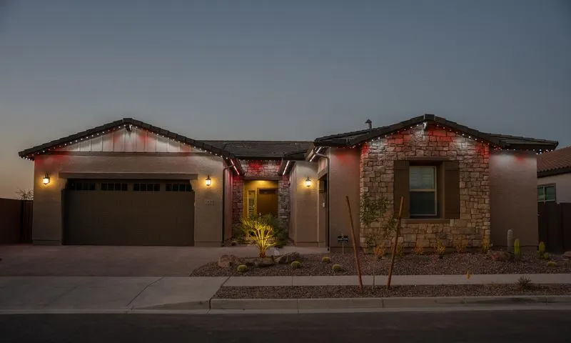 Single-story desert home at twilight with alternating red and warm white permanent lights along the roofline and garage