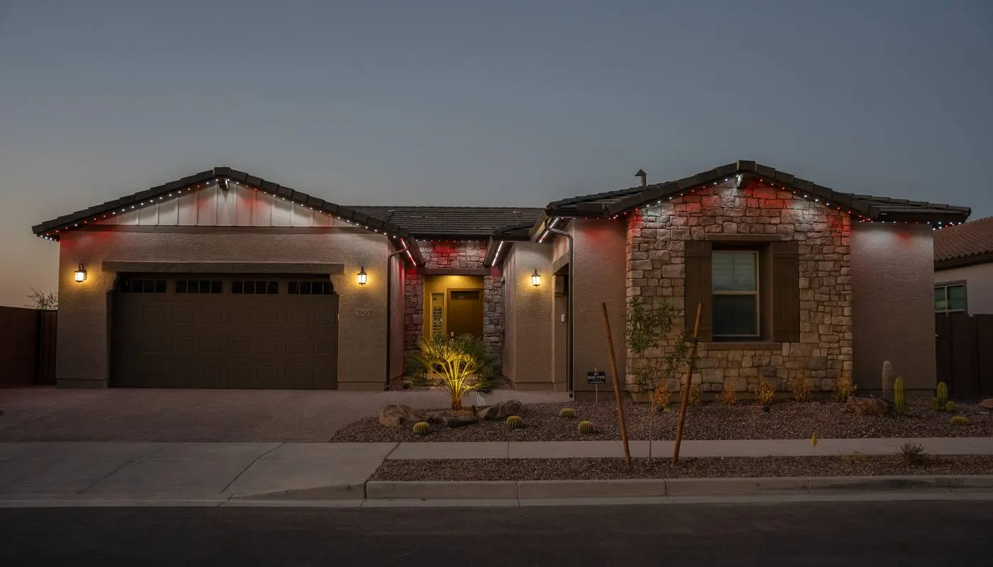 Desert home with alternating red and white permanent roofline lighting and warm uplighting on the stone facade
