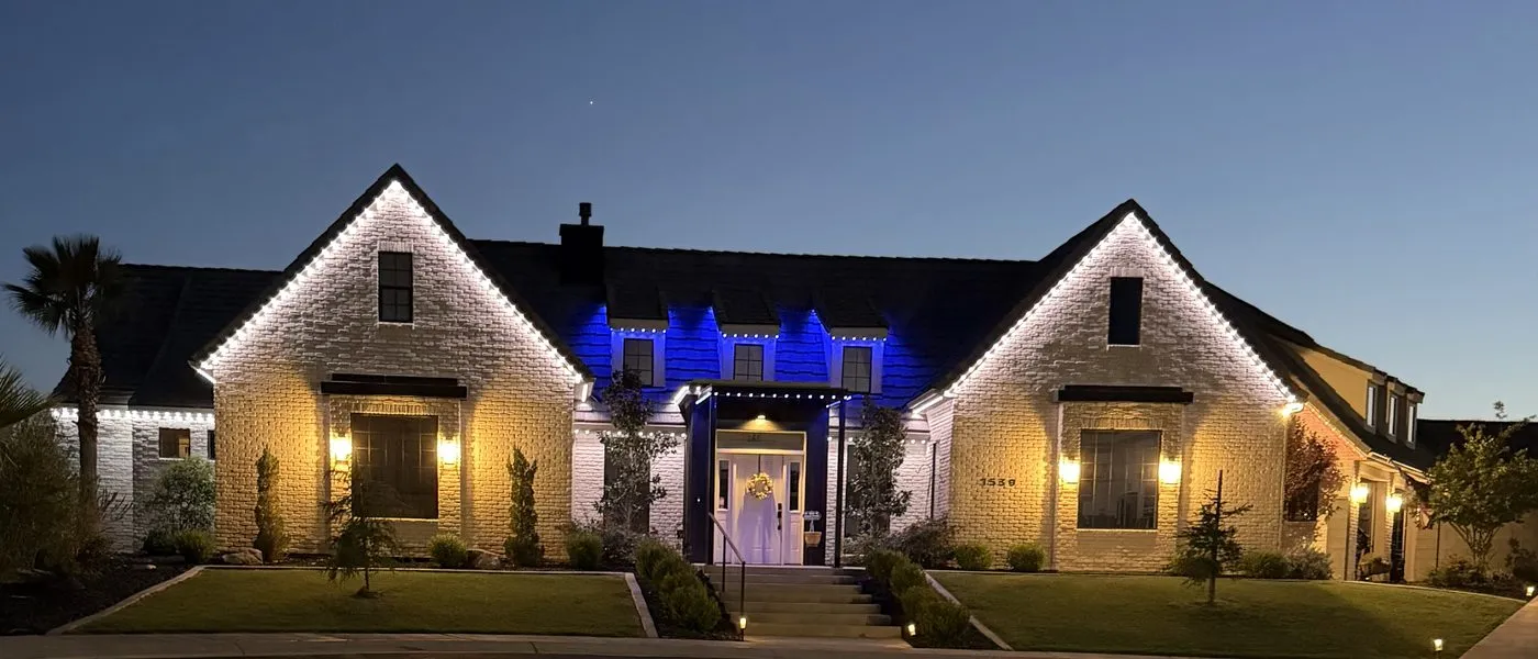 Brick ranch home lit with warm white permanent roofline lighting and a deep blue accent zone over the central entry