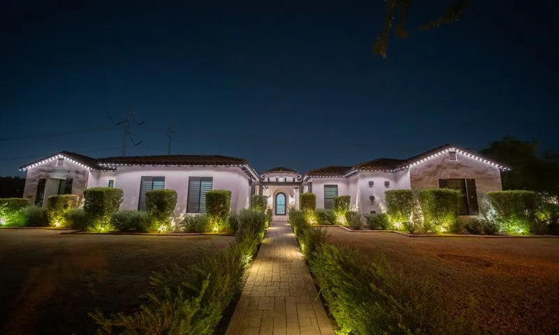 Spanish-style home at night with crisp white permanent roofline lighting and green landscape uplighting on trimmed hedges