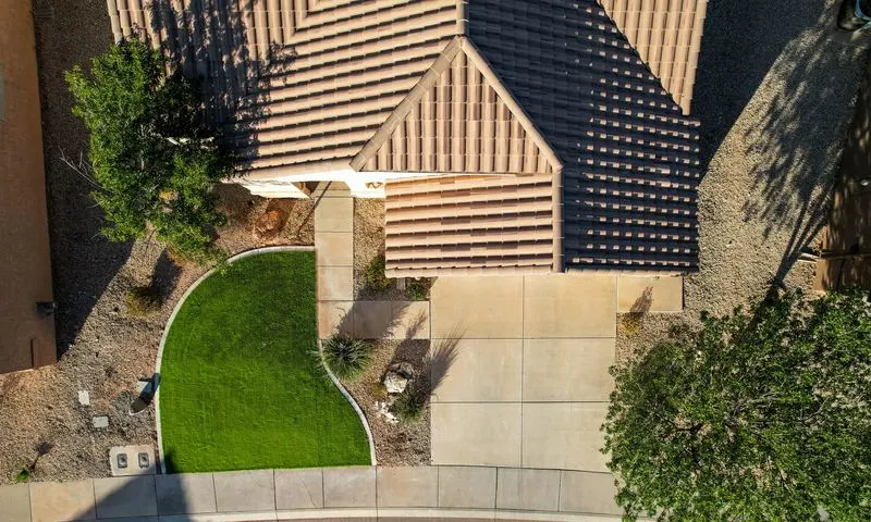 Aerial view of a curved artificial turf lawn with concrete border beside a tile-roof home and gravel desert landscaping