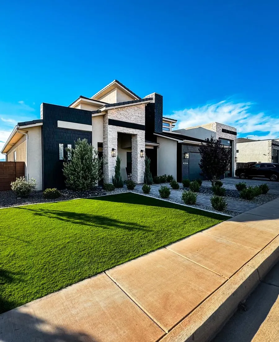 Modern white and dark grey stucco home in St. George with a bright green artificial turf front lawn bordered by paver walkways and desert shrubs